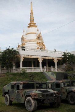 Description: Around the stupa at Wat Lak Muang temple in the southern Thai city of Pattani, prefabricated barracks have been set up for soldiers and armoured vehicles and transport lorries are parked nearby.