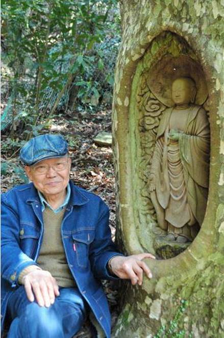 Description: Fumiaki Ogita sits next to his Buddhist statuette he carved out of a live tree in Shikokuchuo, Ehime Prefecture. (Haruko Hosokawa)