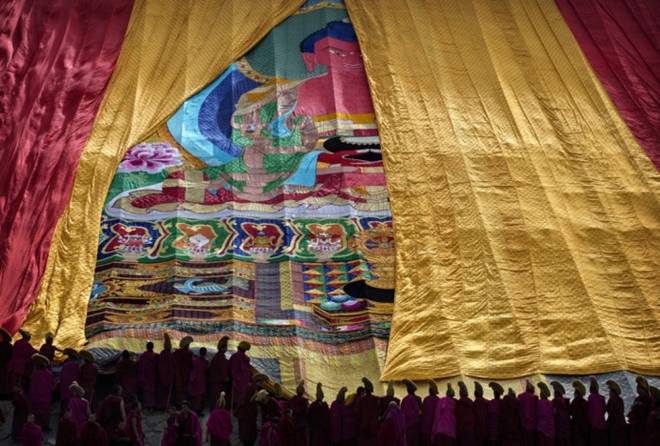 Monks unveil a large thangka, a religious silk embroidery or painting unique to Tibet, showing Buddha.
