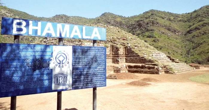 A signboard with information about the Bhamala stupa and monastery in English and Urdu.